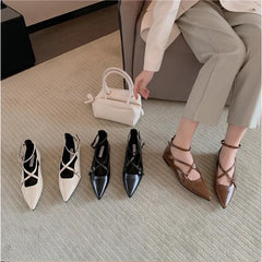 A selection of leather flats displayed in a room with a person standing in a chair in the background, holding a white bag and wearing light-colored trousers.