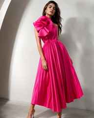 Woman wearing a bright pink dress with a large floral detail on a white background