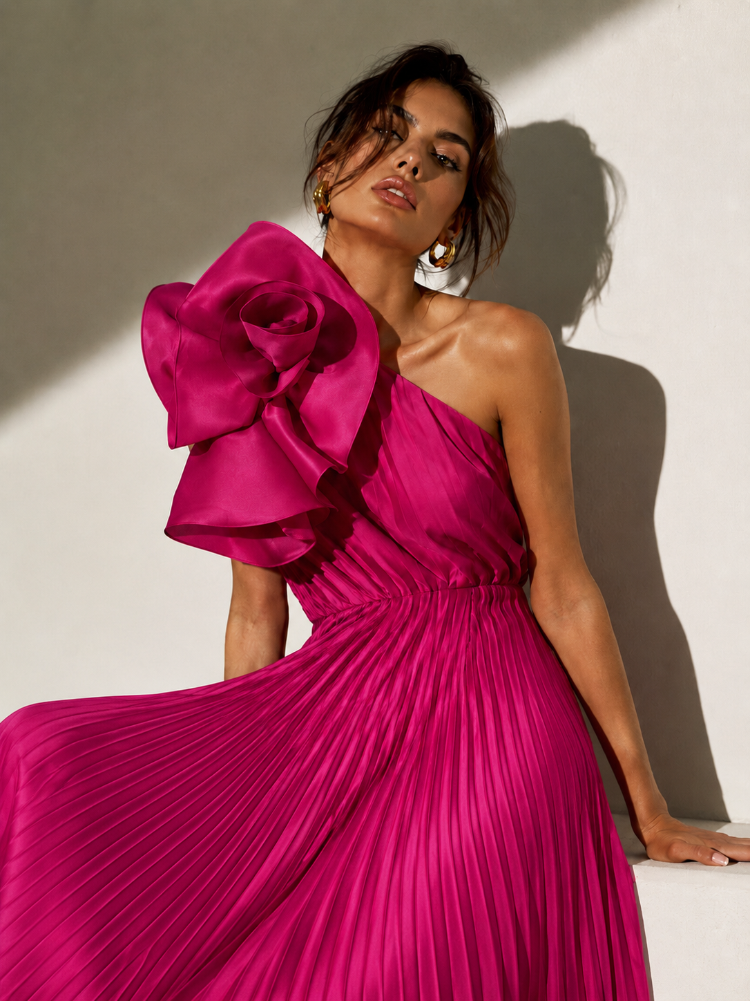 Woman wearing a vibrant pink one-shoulder dress with a large floral detail against a neutral background.